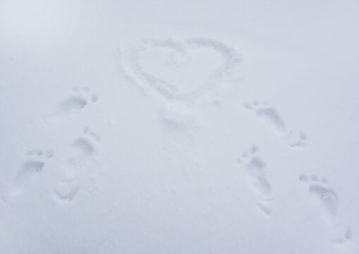 Traces, prints of bare feet in the snow lead to the painted heart. Background for Valentine's Day cards.