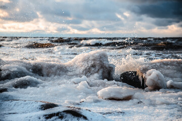 Sunlight shines on the sea waves. The wind blows the waves ashore. In winter, the embankment is icy with stones