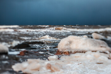 Sunlight shines on the sea waves. The wind blows the waves ashore. In winter, the embankment is icy with stones