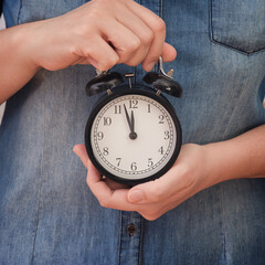 A woman holding an alarm clock that is showing a few minutes before twelve in her hands. Few...