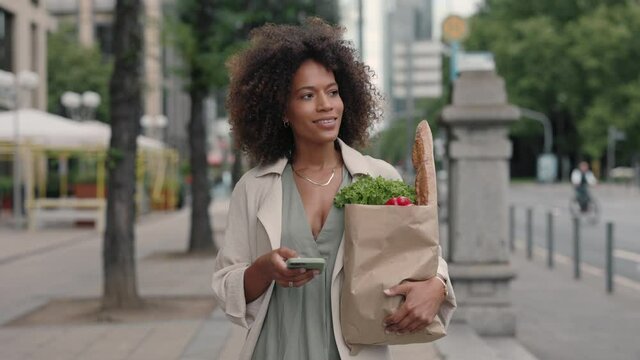 Woman using mobile walking on street with grocery bag