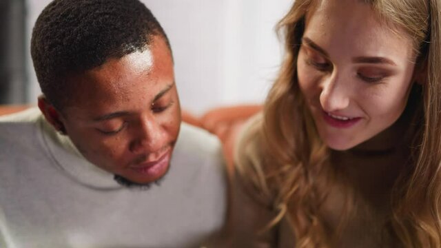 Pretty young white woman talks to nodding African-American man groupmate spending time together in living room close view slow motion