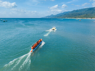 Aerial of a speedboat towing a banana boat near the beach. In Laiya, San Juan, Batangas, Phillipines.