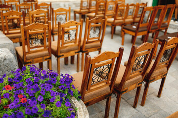 Fototapeta na wymiar Wooden chairs with patterns on the backs stand in rows on paving stones