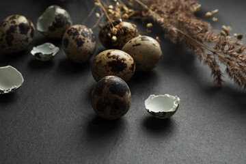 Small spotted eggs and dry pampas grass stems scattered on dark table surface easter concept