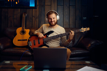 Man playing guitar listening looking at laptop