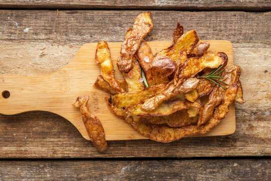 Crispy fried potato peel chips with rosemary and salt, top view, wooden background.