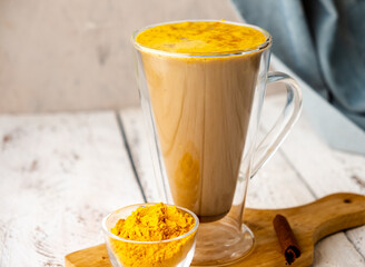 A healthy drink golden latte with turmeric in a large glass. Golden milk with spices. White table.