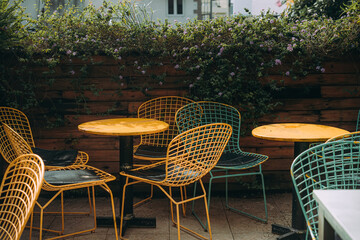 Wicker chairs made of wire stand near a tree on a tile. Nobody is there, unusual chairs are...