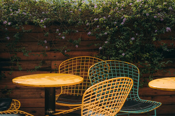 Wicker chairs made of wire stand near a tree on a tile. Nobody is there, unusual chairs are standing in a garden. Arm chairs with metal legs.