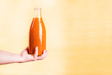 yellow, wooden background. a glass bottle with an orange liquid inside. the juice of tangerine and...