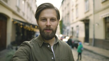 Portrait of cheerful young man looking at camera and talking recording vlog. POV of handsome young bearded man making online video call looking at camera. High quality 4k footage