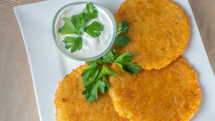 Close-up view of fried potato pancakes with cream sauce and leaf of parsley.