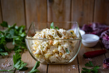 Hearty snack: salad with fish and vegetables with mayonnaise in a glass plate on a wooden table. Close-up
