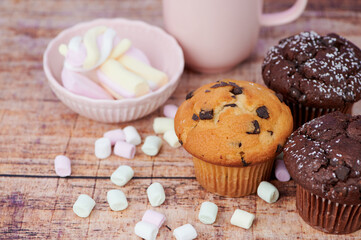 three muffins with pastel colored marshmallows and a mug on wooden background