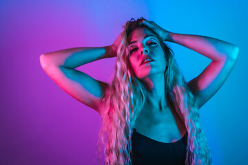 Portrait of a Caucasian blonde girl with eye drawing makeup, groomed eyelashes on a blue background with pink neon lights