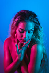 Portrait of a Caucasian blonde girl with eye drawing makeup, groomed eyelashes on a blue background with pink neon lights