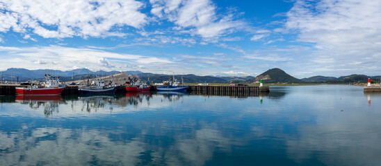 Paisaje panorámico del puerto de Santoña, con barcas de pesca amarradas y reflejos en el mar azul con nubes blancas en Cantabria , España verano de 2020