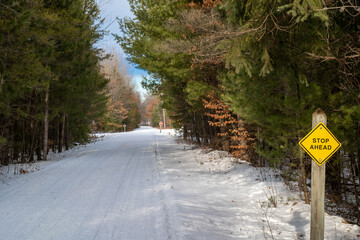 Stop ahead sign on a snow covered snowmobile and hiking trail through a forest in Central Minnesota. Paul Bunyan State Trail in Nisswa.