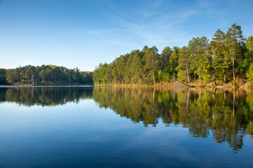 Beautiful calm northern Minnesota lake under blue sky with trees along the shore in afternoon sunlight © Daniel Thornberg