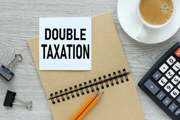 Double Taxation. text on white sticker on wood table