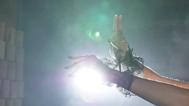 Actress hands in lacy cuffs gesticulate slowly in smoke cloud against studio wall with fixed books at artificial back light closeup