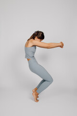 Fototapeta na wymiar Sporty young woman does yoga. Concept of healthy lifestyle, brunette in fitness suit stands in yoga pose on isolated background, smiles and shows her flexibility, side view. 
