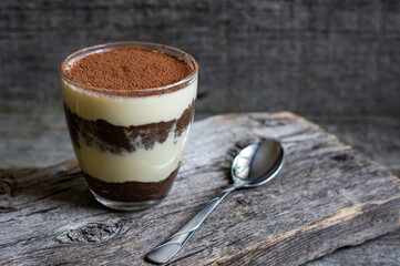 Tiramisu, traditional italian dessert in glass on wooden background. Selective focus
