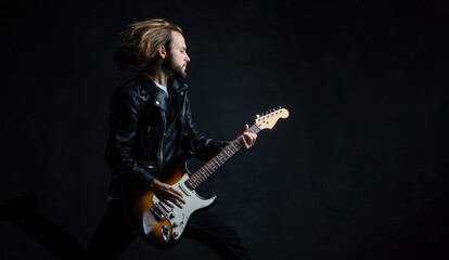 emotional musician playing electric guitar in leather jacket and jumping, copy space, guitarist.