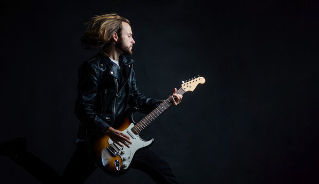 emotional musician playing electric guitar in leather jacket and jumping, copy space, guitarist.