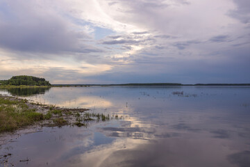 Fototapeta premium Evening landscape on the lake in early spring. The dramatic sky is reflected in the water.