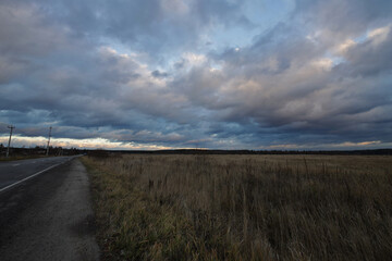 Evening landscape with a road going beyond the horizon. Autumn dramatic sky with clouds. The colorful sky in the evening light. Rural landscape.