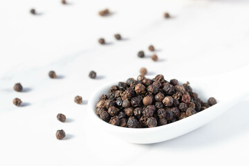 black peppercorns in a spoon on white