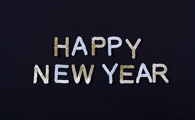 Inscription of "Happy New Year" embroidered with silver and golden sequins on black textured background as holiday decoration