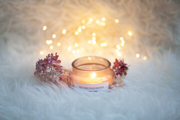 Burning candle in a glass jar. Soft fluffy blanket. White woolen blanket. bokeh in the background. 