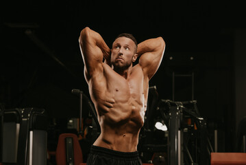 Fototapeta na wymiar A bodybuilder with a beard is doing a stomach vacuum pose during a workout.