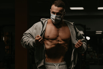 Fototapeta na wymiar A bodybuilder in a face mask is opening his hoodie to demonstrate his vacuum.