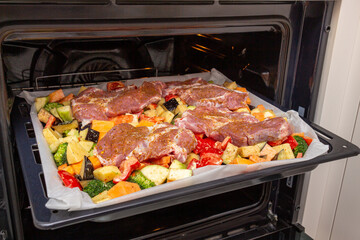 Finely chopped and seasoned vegetables with pork, placed on a baking sheet, before baking on parchment in the oven. Potatoes, bell peppers, squash, pumpkin and broccoli. Close-up
