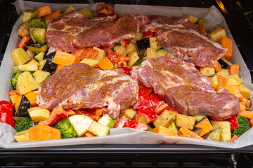 Finely chopped and seasoned vegetables with pork, placed on a baking sheet, before baking on parchment in the oven. Potatoes, bell peppers, squash, pumpkin and broccoli. Close-up