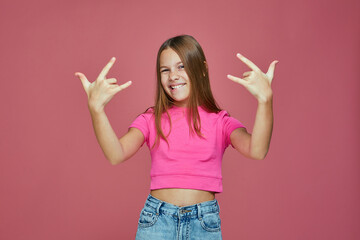 Cool naughty child girl tomboy show rock, heavy metal gesture by hands, having fun on pink studio...
