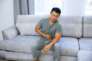 Casual man sitting on a couch at home complaining suffering belly ache