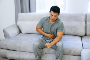 Obraz premium Man suffering from abdominal pain, diarrhea, discomfort while sitting on sofa in living room at home