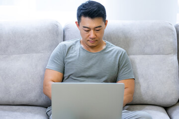 beautiful concentration young man indoors at home on the couch using a laptop computer, working from home, distance learning