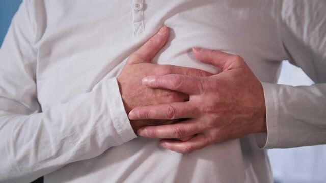 health care, heart attack or painful cramps in older man, pensioner holding his chest with both hands close up