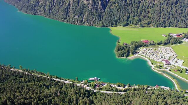 aerial panoramic video of north part of Achen lake near Achenkirch in Tirol during sunny summer day with a ferry boat leaving the boat stop Scholastika - the camp ground is located close to the lake 