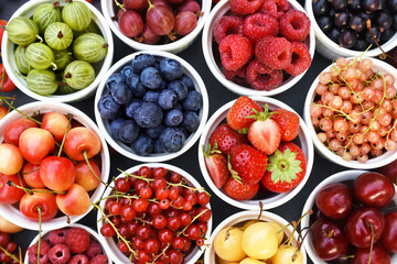 Fresh ripe organic fruits and berries in bowls from market: strawberry and raspberry, currant and blueberry; healthy fruit and berry background