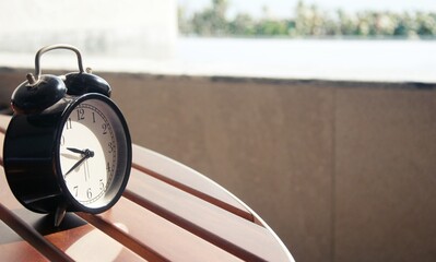 Retro alarm clock on table at outdoor patio with sun light blurred  background , interior object...