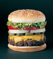 Classic cheeseburger with beef patty, pickles, cheese, tomato, onion, lettuce and ketchup mustard isolated on black background.