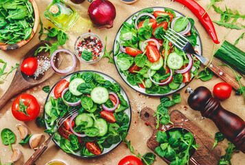 Spring vegetable salad with green spinach, red tomatoes, cucumber, corn salad and onion. Healthy vegan food. Stone kitchen table background. Top view