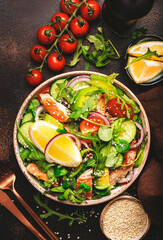 Fresh Salad with chicken, tomatoes, arugula, onion, avocado, sesame seeds and lemon oil dressing. Healthy food. Top view. Brown table